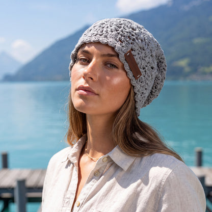 Woman wearing a gray handmade crochet slouchy beanie by YarnYummies on a lakeside dock with mountains in the background