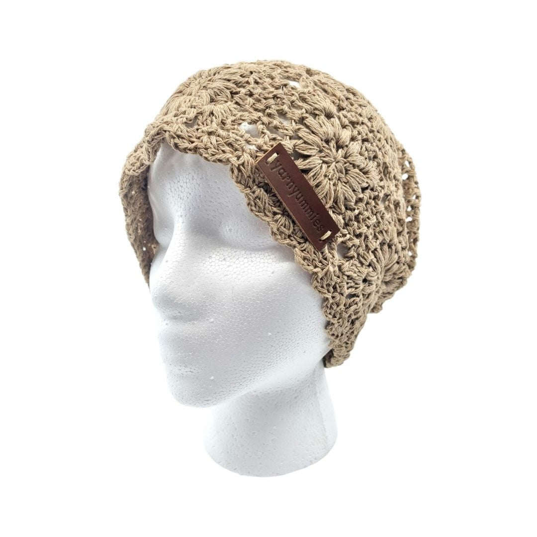 Beige crochet hat with brown leather strap on a mannequin head against a white background
