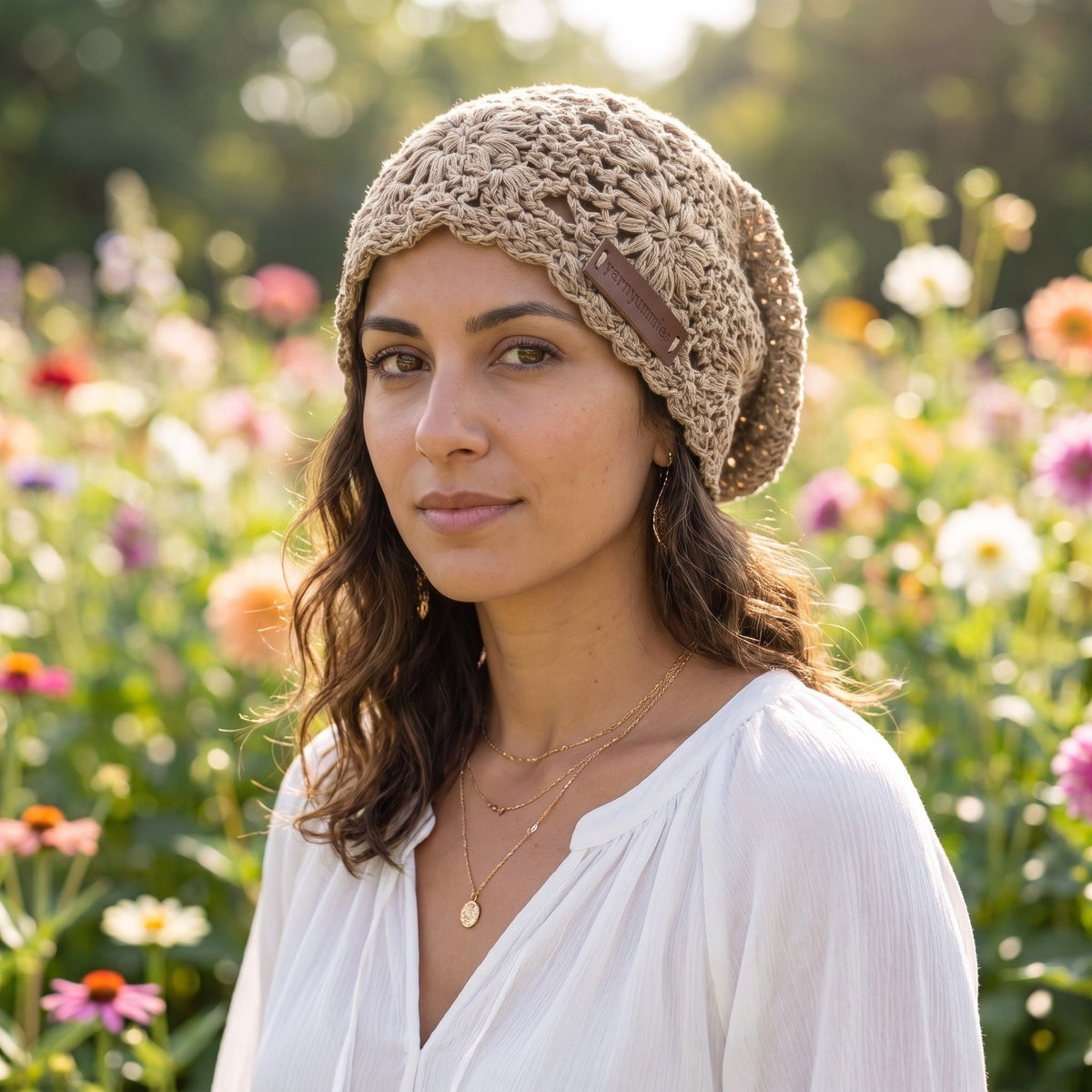 Woman wearing a khaki handmade crochet slouchy beanie hat by YarnYummies in a sunlit flower garden