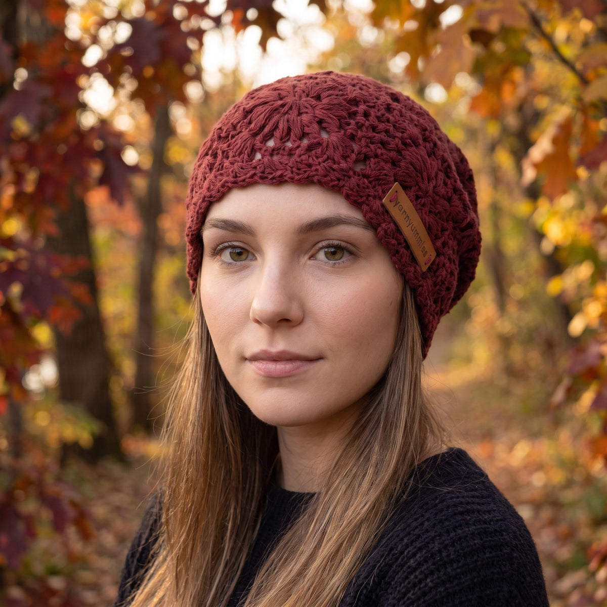 Woman wearing a burgundy handmade crochet slouchy beanie by YarnYummies outdoors in an autumn forest setting