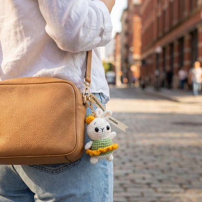 Person holding a brown leather bag with a plush keychain attached, walking down a street.