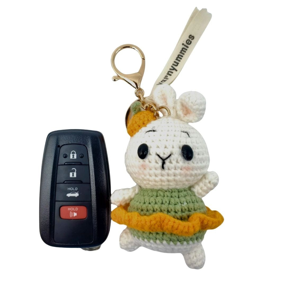Crocheted keychain of a white character with a yellow scarf next to a car key fob on a white background.