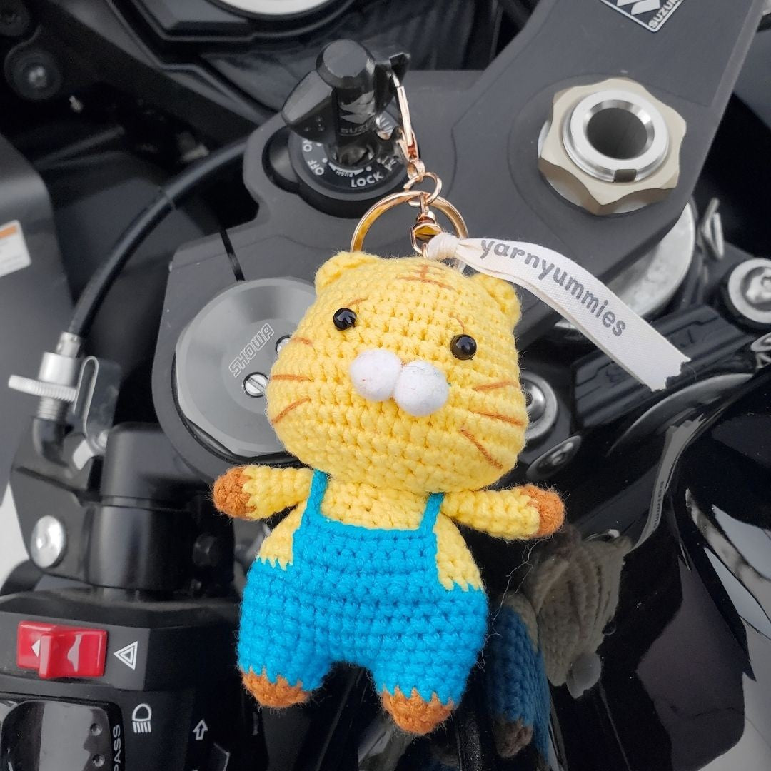 Crocheted cat keychain with blue overalls attached to a motorcycle.