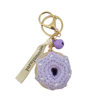 Purple donut-shaped crocheted keychain with gold tag and purple bead on a white background