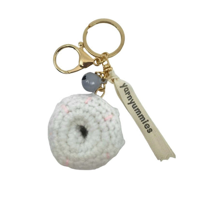 Donut-shaped crocheted keychain with a textured ball charm and 'yummyummies' tag on a white background