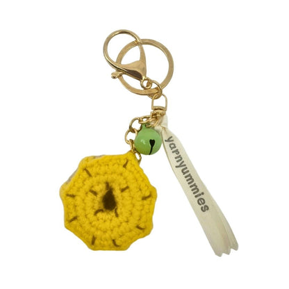 Yellow donut-shaped crocheted keychain with a green bead and 'Yarnyummies' tag on a white background