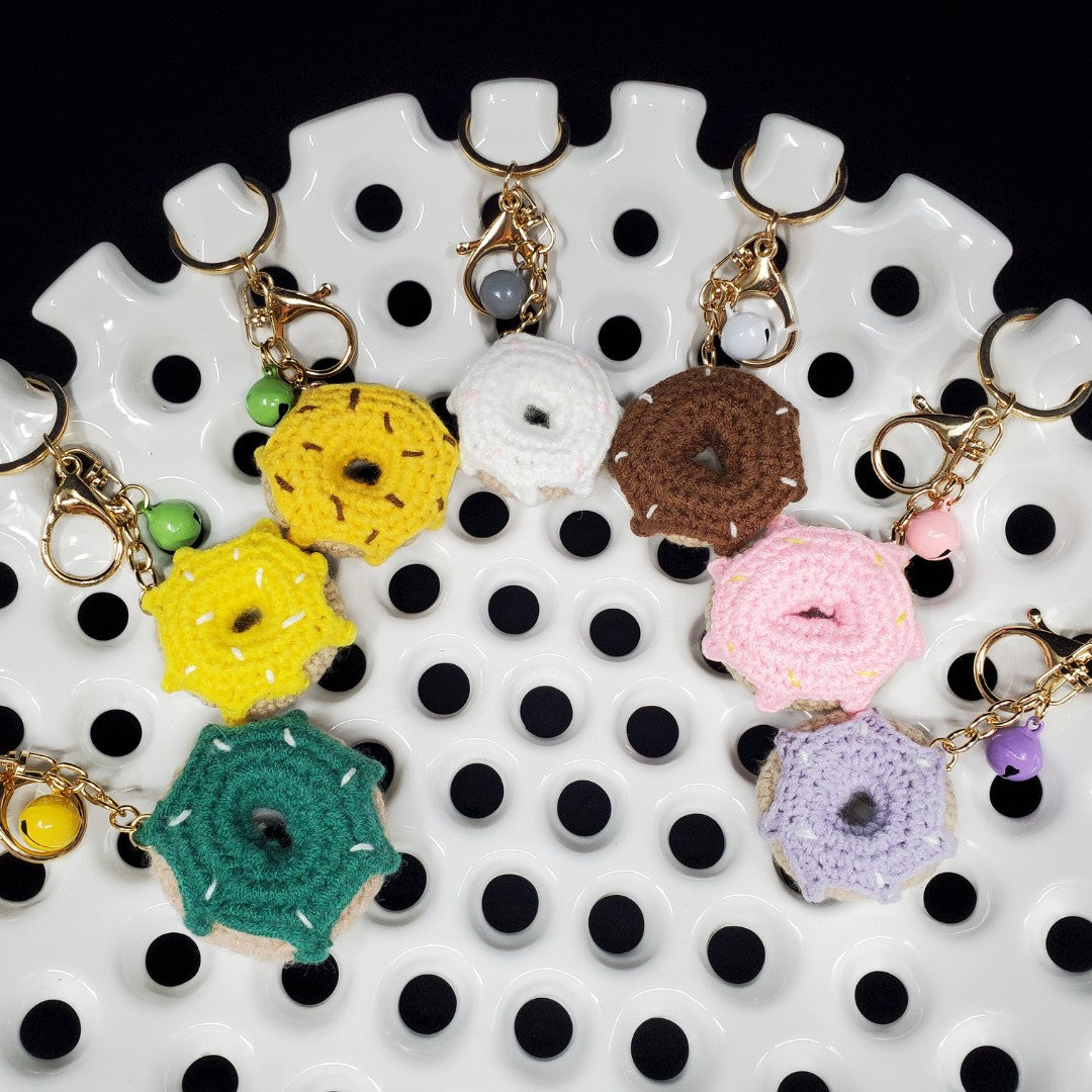Colorful donut-shaped crocheted keychains on a white and black polka dot surface