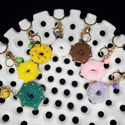 Colorful donut-shaped crocheted keychains on a white and black polka dot surface