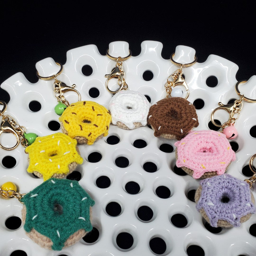 Colorful crocheted donut keychains on a white and black patterned surface