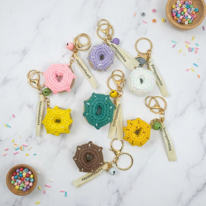 Colorful donut-shaped crocheted keychains on a marble surface with sprinkles and beads.