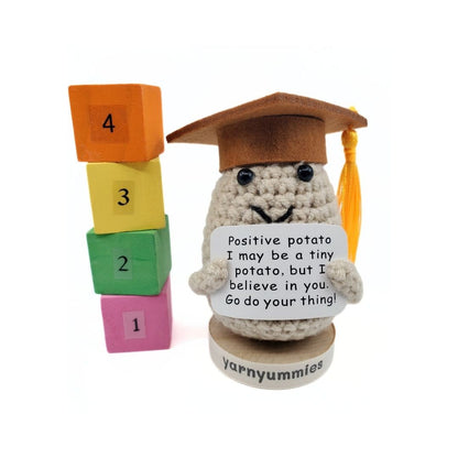Crocheted potato character in a graduation cap with number blocks and a motivational sign, branded 'yarnyummies'.