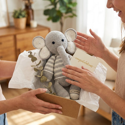 Person receiving a knitted elephant toy as a gift in a box with a 'congratulations' card.