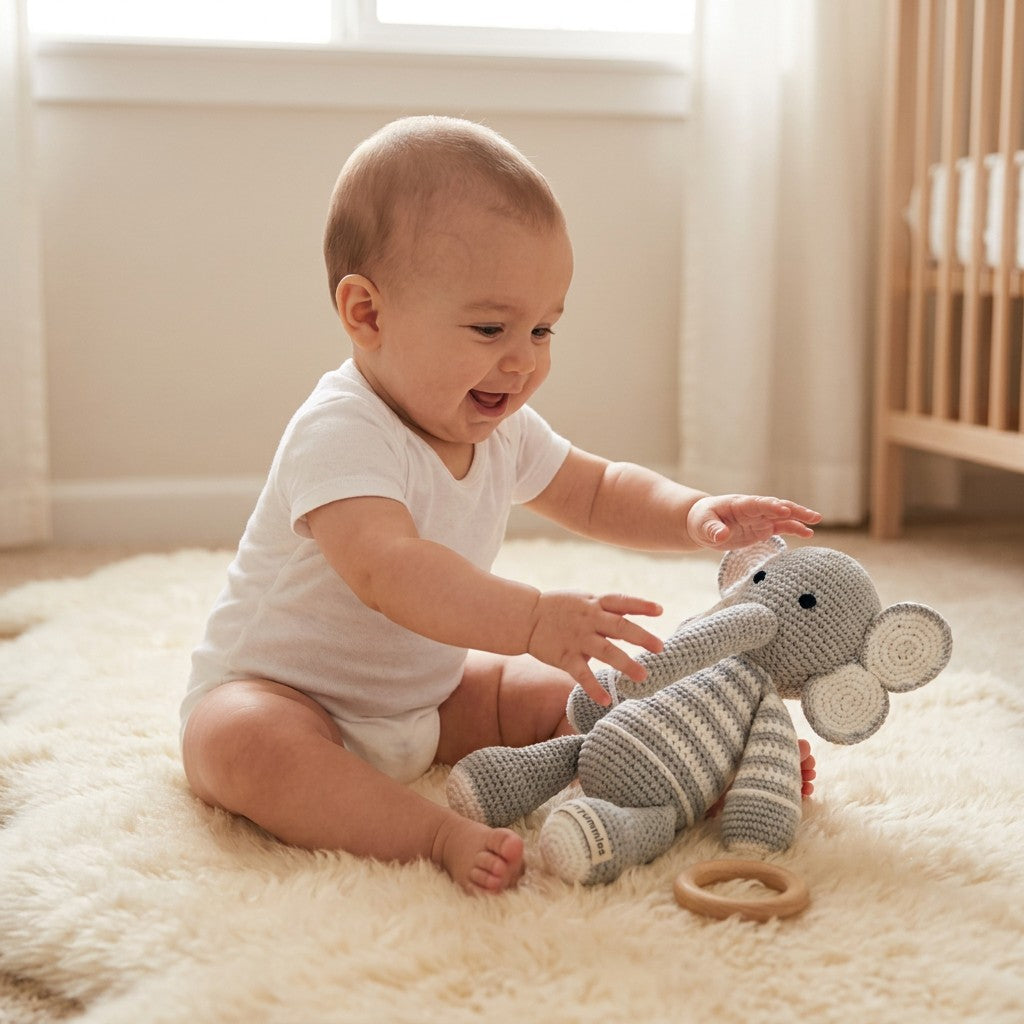 Baby playing with a knitted elephant toy on a soft surface