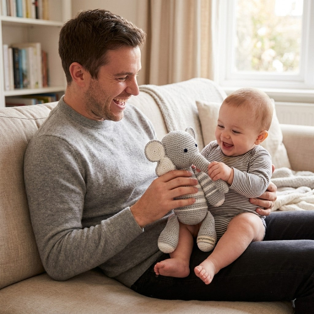 Man and baby sitting on a couch with a toy elephant, smiling.