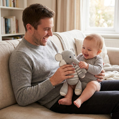 Man and baby sitting on a couch with a toy elephant, smiling.