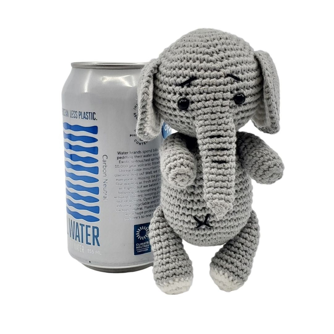Crocheted elephant toy next to a can of water on a white background