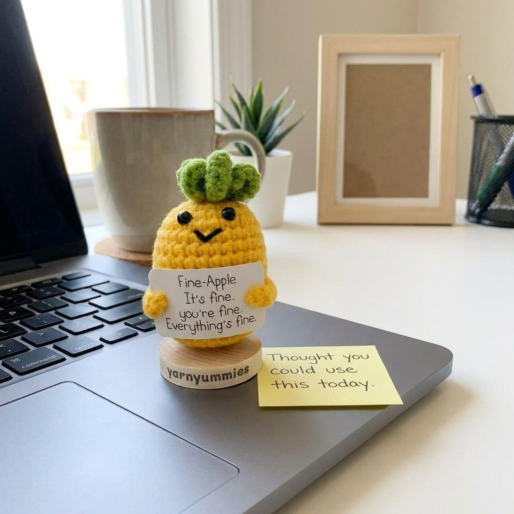 Crocheted pineapple plush decor with a message on a desk next to a laptop