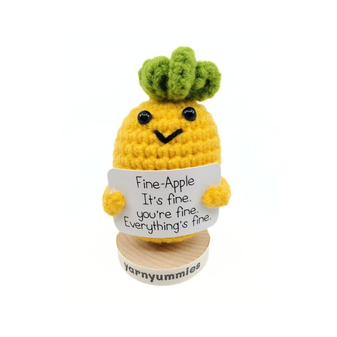 Crocheted pineapple character holding a sign with text, on a white background