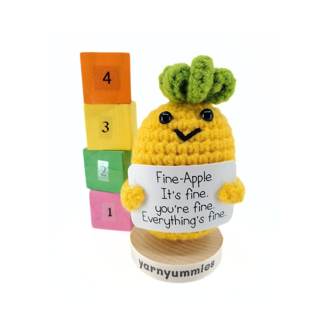Crocheted pineapple plush with a sign and number blocks on a white background