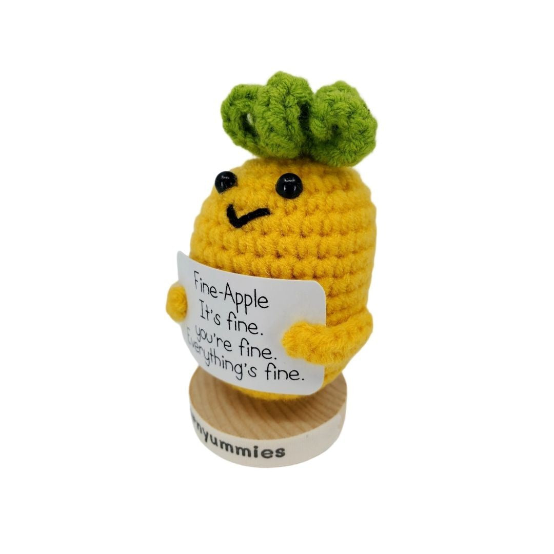 Crocheted pineapple character holding a sign with text, on a white background