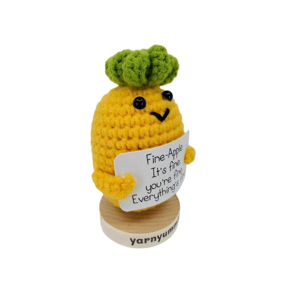 Crocheted pineapple character plush holding a sign with text on a white background