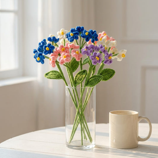 Vase with colorful knitted flowers on a table next to a mug.