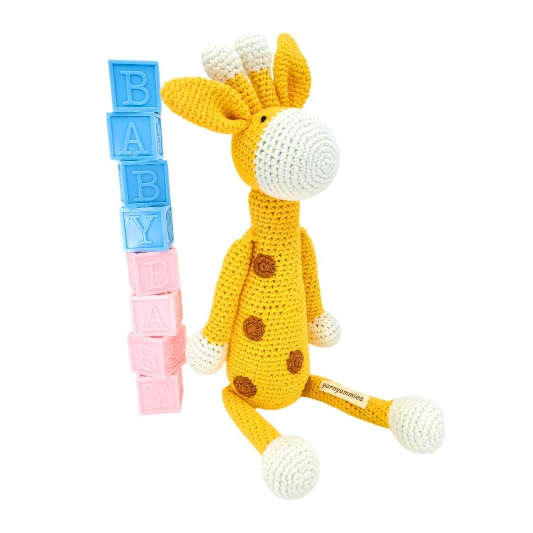 Crocheted giraffe toy with 'BABY' blocks on a white background