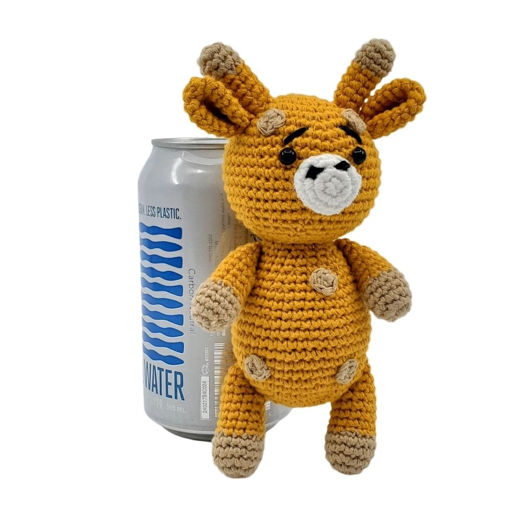 Crocheted giraffe toy next to a can of water on a white background