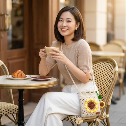 Woman sitting at a cafe table with a cup of coffee and a crocheted sunflower-patterned bag.