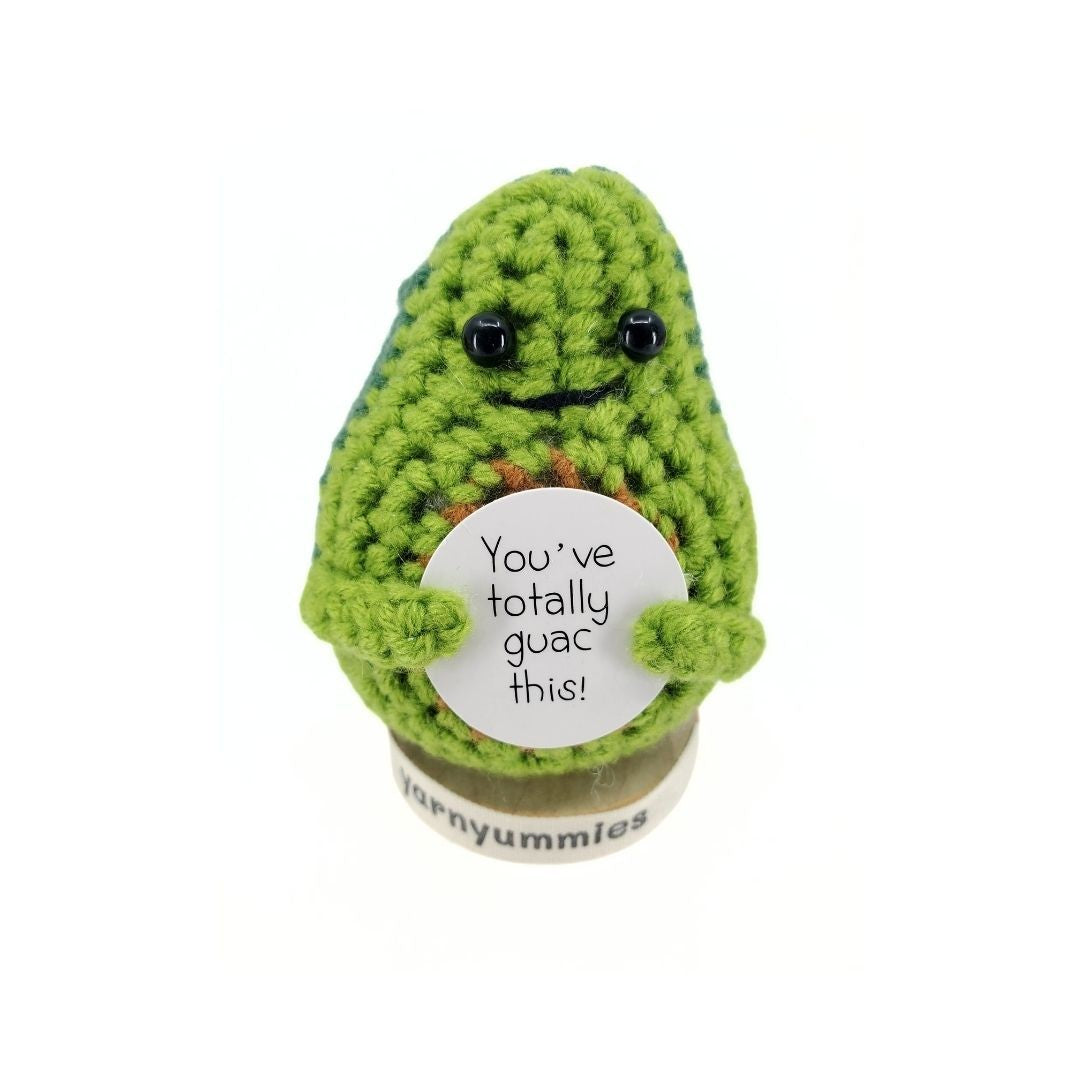 Crocheted avocado plush decor holding a sign with text on a white background