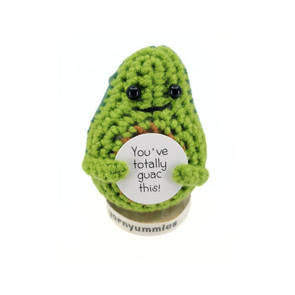 Crocheted avocado plush decor holding a sign with text on a white background
