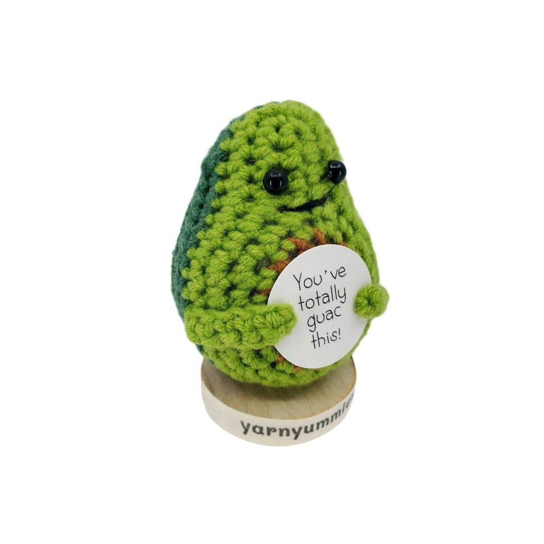 Crocheted avocado plush decor holding a sign with text, on a white background