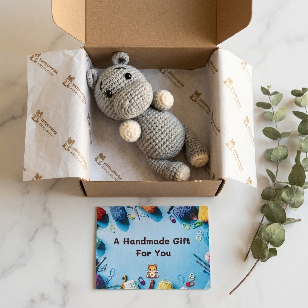 Handmade crochet hippo toy in a box with a 'Handmade Gift For You' card on a marble surface.