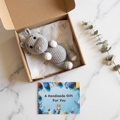 Crocheted animal toy in an open box with a 'Handmade Gift' card on a marble surface.