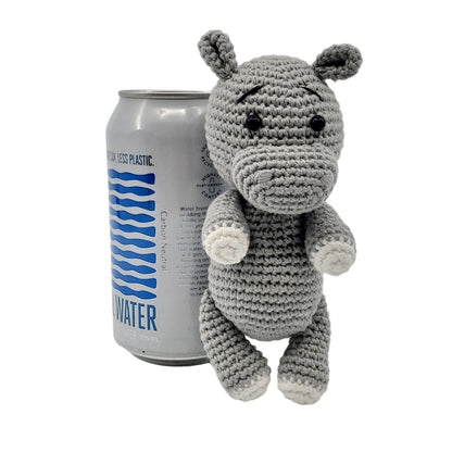 Crocheted hippo toy next to a can of water on a white background