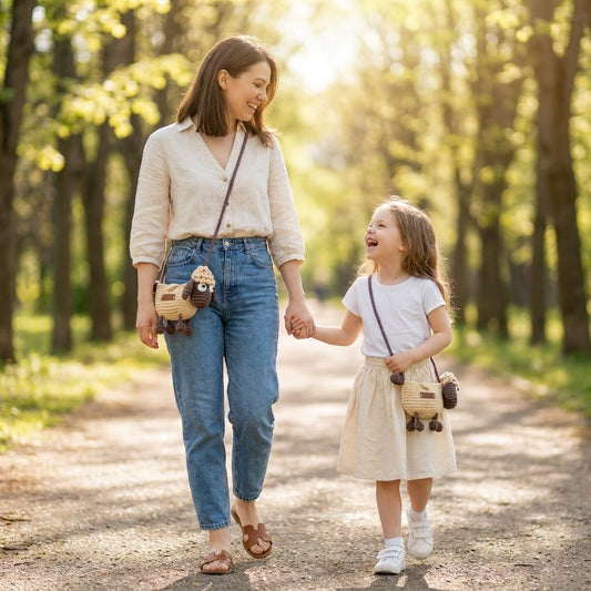 Woman and child walking hand-in-hand on a path in a park wearing the same crocheted crossbody sheep designed bag.