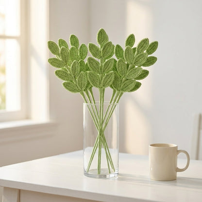 Green leafy branches in a clear vase on a white surface with a light background