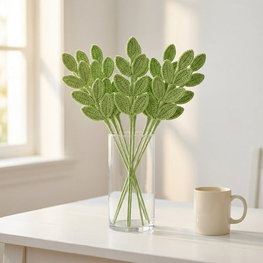 Green leafy branches in a clear vase on a white surface with a light background