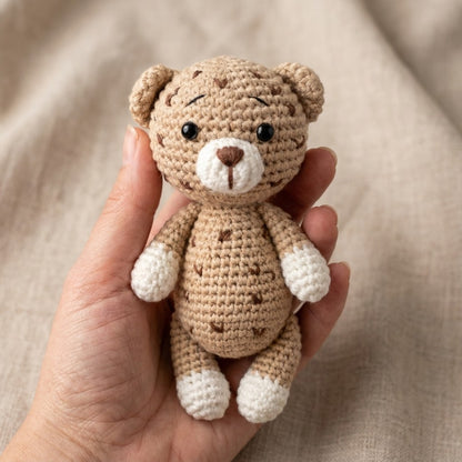 Hand holding a small crochet leopard against a neutral background