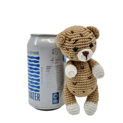 Crocheted leopard next to a can of water on a white background