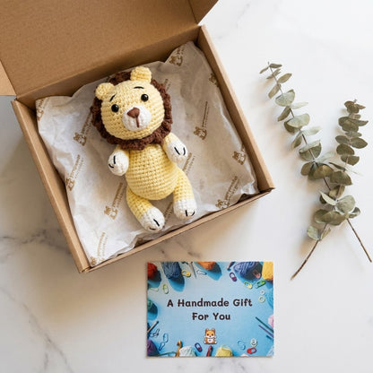 Crocheted lion toy in a box with a card reading 'A Handmade Gift For You' on a marble surface.