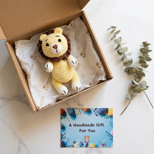Crocheted lion toy in a box with a card reading 'A Handmade Gift For You' on a marble surface.