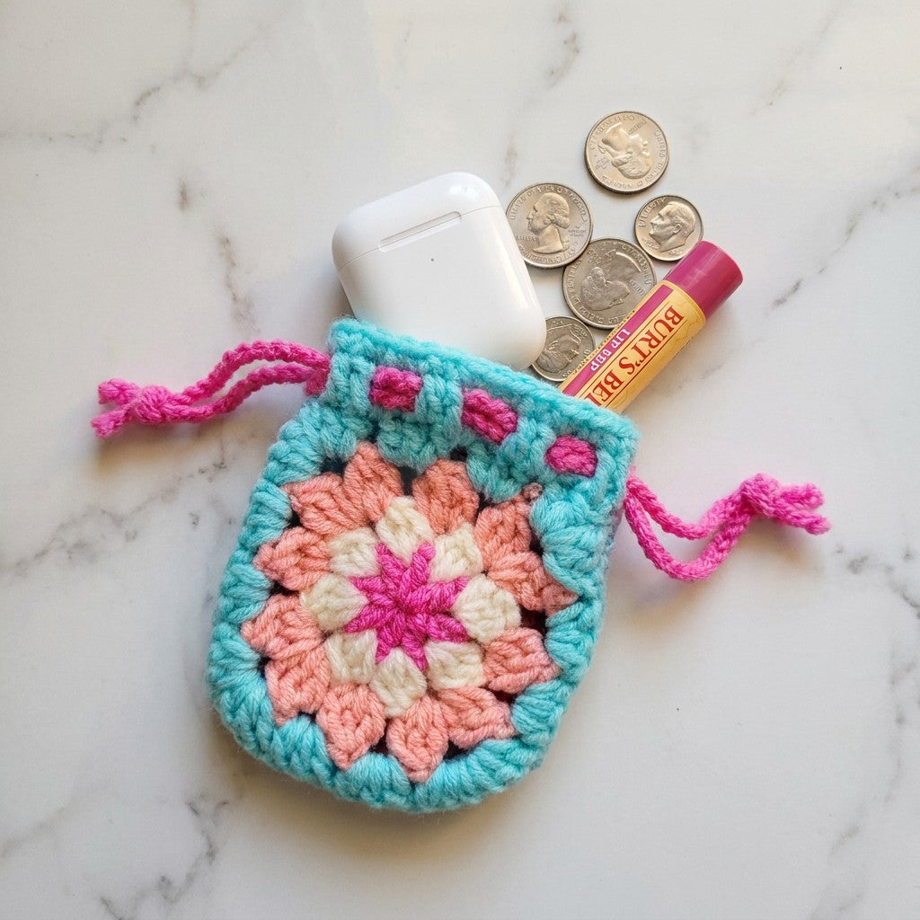 Crocheted pouch with colorful pattern on a marble surface with lip balm and coins.