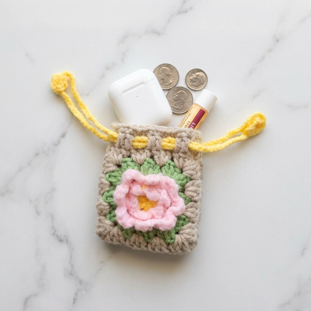 Crocheted pouch with a pink flower design on a marble surface