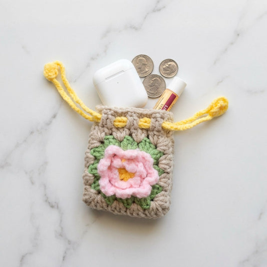 Crocheted pouch with a pink flower design on a marble surface