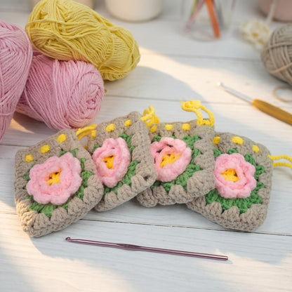 Four crocheted flower patterned mini purses with yarn and a crochet hook on a wooden surface