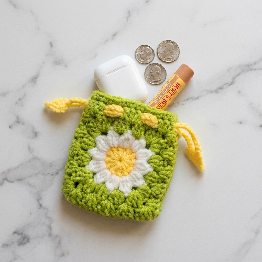 Green crochet pouch with a white flower design on a marble surface with coins and a lip balm.
