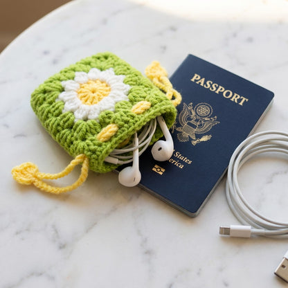 Green crochet pouch with white flower design, passport, and cables on a marble surface