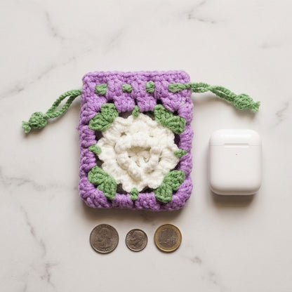 Crocheted pouch with a floral design on a marble surface with coins and a white device.