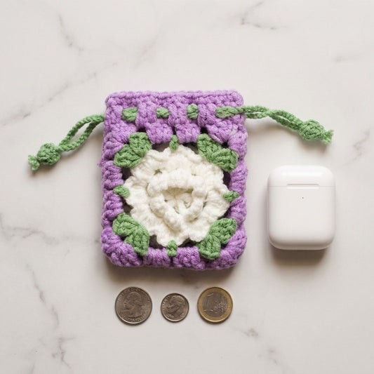 Crocheted pouch with a floral design on a marble surface with coins and a white device.
